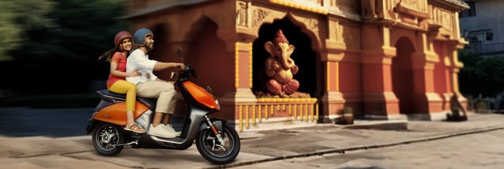 An image showcasing a couple riding VIDA electric scooters near Ganpati Pandal in Ganesh Chaturthi festival.